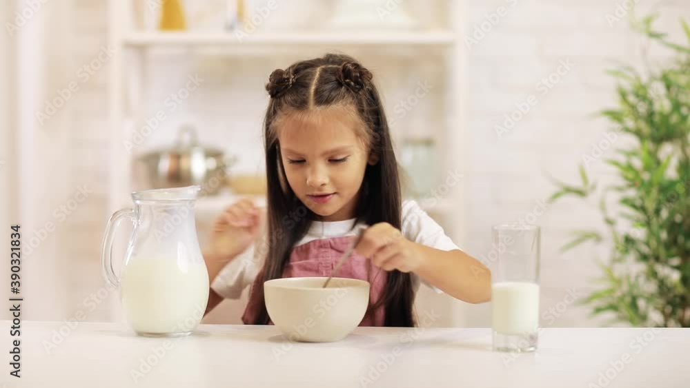 child pours milk into a bowl of cereal in the kitchen. cute little girl eating breakfast: cereal with the milk. healthy breakfast child pours milk into a bowl of cereal in the kitchen. cute little girl eating breakfast: cereal with the milk. healthy breakfast