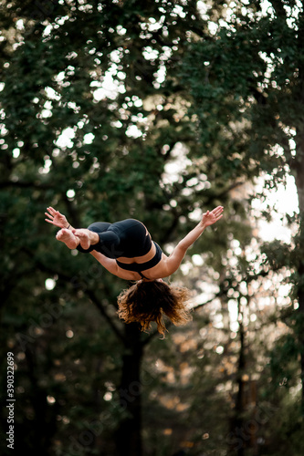 view of woman jumping high in the air against background of green trees