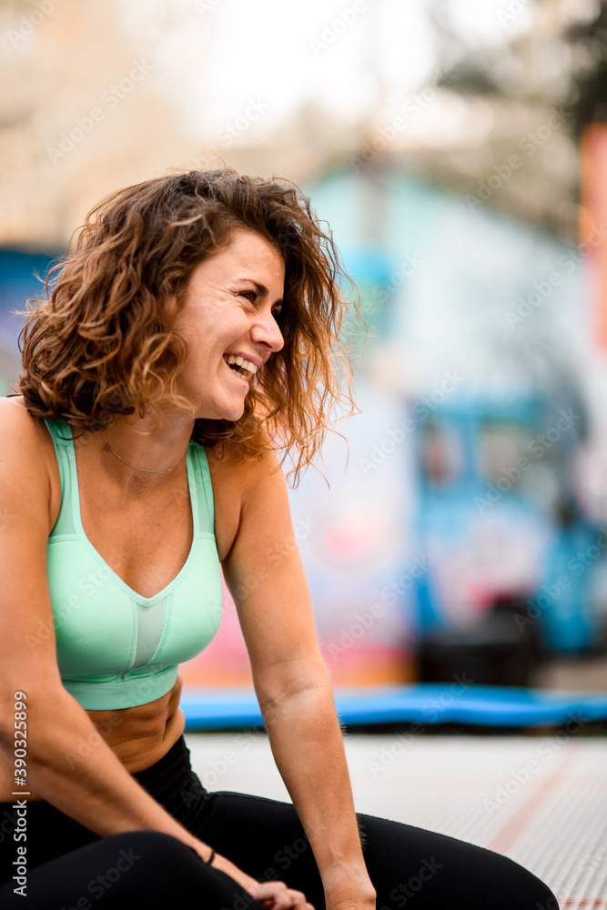 cheerful woman with curly hair in bright sports top sitting on trampoline cheerful woman with curly hair in bright sports top sitting on trampoline