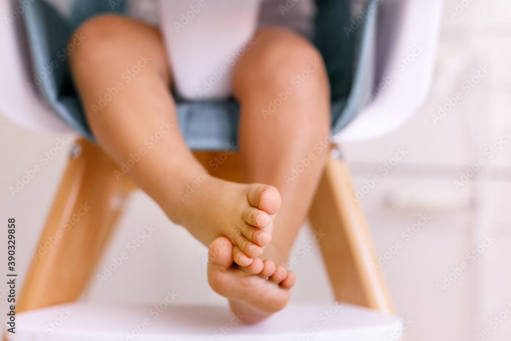 One years old child's feet on high chair while he is eating at kitchen dinner table.