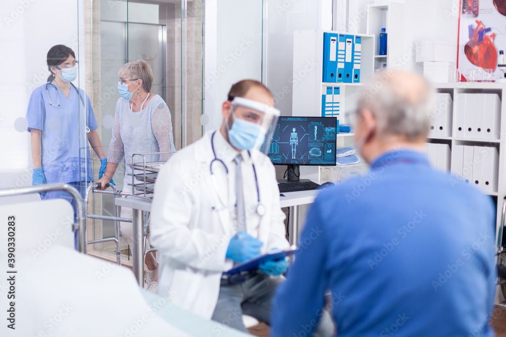 Nurse helping disabled old woman with walking frame on hospital corridor. Modern private clinic. Practitioner physician appointment. Doctor with face mask against covid. Nurse helping disabled old woman with walking frame on hospital corridor. Modern private clinic. Practitioner physician appointment. Doctor with face mask against covid.