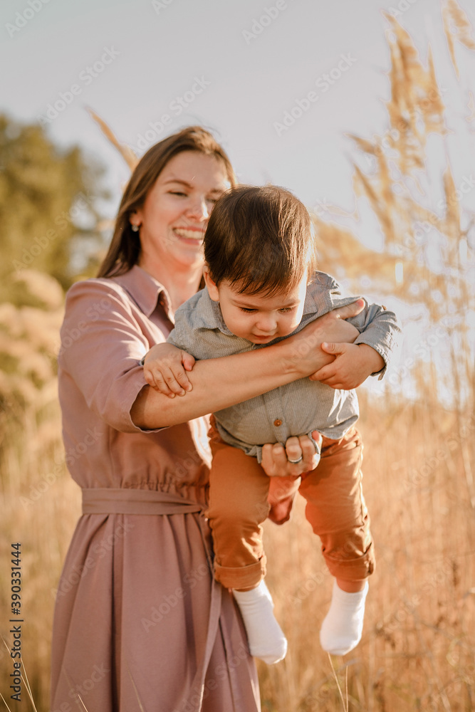 Fototapeta premium Portrait of happy loving mother hugging her baby son in the sunny park near river
