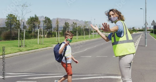 Caucasian female teacher wearing a face mask and high visibility vest stopping traffic on a pedestri