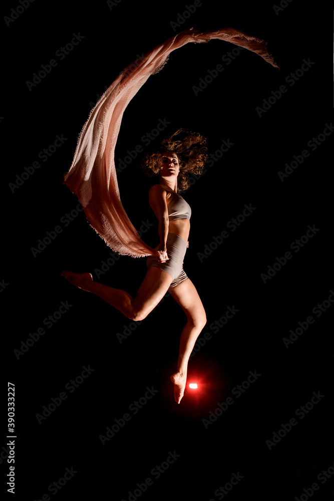 woman jumps high in the air and does trick with pink scarf in the dark.