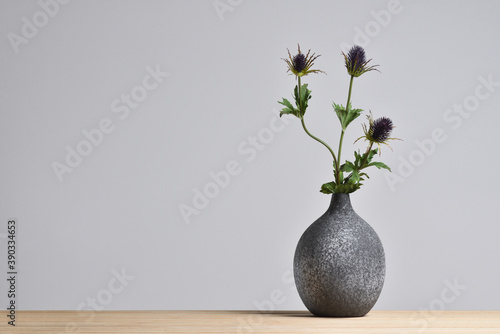 Modern ceramic vase with thistle flower on gray background