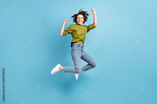 Photo portrait of crazy ecstatic woman jumping up celebrating fists in air isolated on pastel light blue colored background