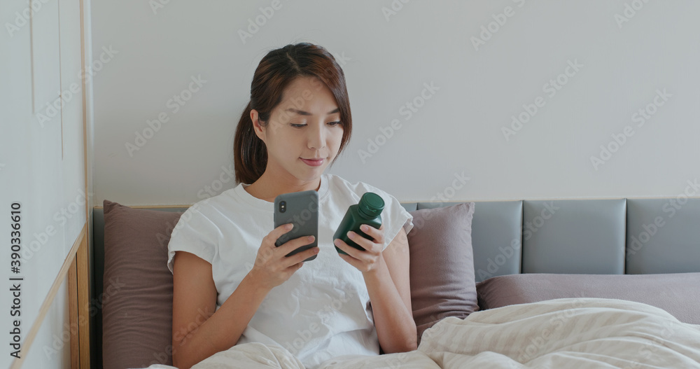 Woman check a bottle of medicine on cellphone and lying on bed Woman check a bottle of medicine on cellphone and lying on bed