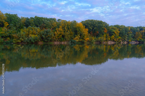 colorful autumn forest landscape in the evening - trees near river and blue sky