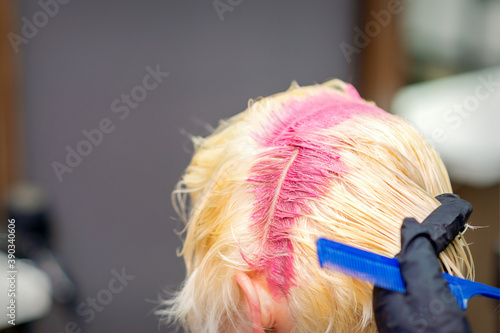 Hair coloring in pink color on hair roots of young blonde woman in hair salon