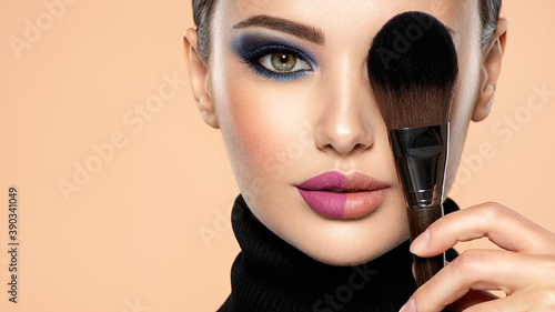 Portrait of a girl with cosmetic brush at face. Woman covering one eye on the face using makeup brush. One half face of a beautiful white woman with  bright makeup and the other is natural. photo