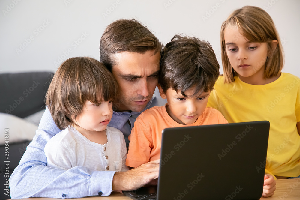 Concentrated father and serious kids looking at screen. Caucasian middle-aged dad typing on laptop screen and children watching his work. Fatherhood, childhood and digital technology concept Concentrated father and serious kids looking at screen. Caucasian middle-aged dad typing on laptop screen and children watching his work. Fatherhood, childhood and digital technology concept