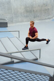 Young Man Stretching Near Concrete Steps Outdoors. Handsome Caucasian Sportsman With Strong Muscular Body In Fashion Sportswear Warming Up Before Intense Workout.