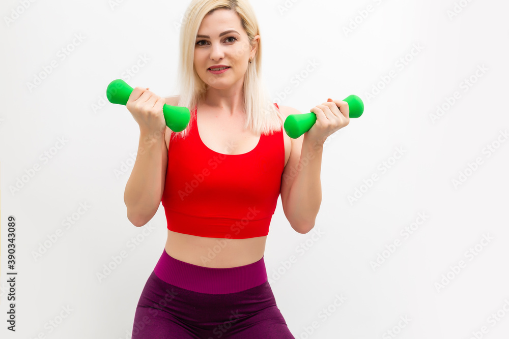 Smiling athletic woman pumping up muscles with dumbbells on white background Smiling athletic woman pumping up muscles with dumbbells on white background