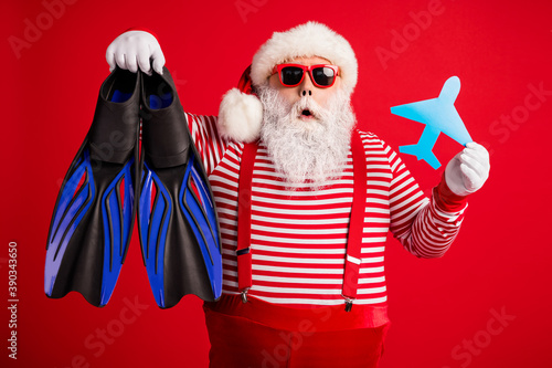 Photo of grandfather grey beard hold paper plane diving flippers shock wear santa claus x-mas costume suspenders sunglass striped shirt cap isolated red color background © deagreez