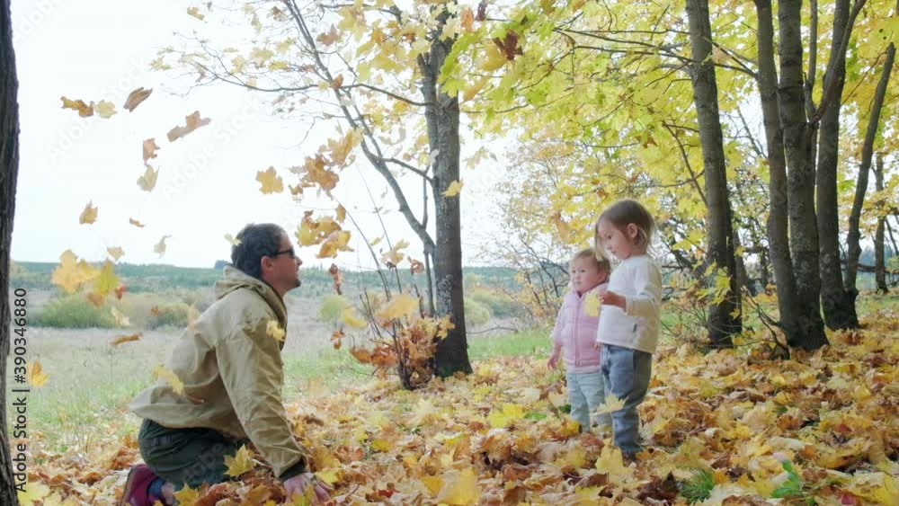 Man throws autumn leaves in front of two toddler girls in an autumn forest Man throws autumn leaves in front of two toddler girls in an autumn forest