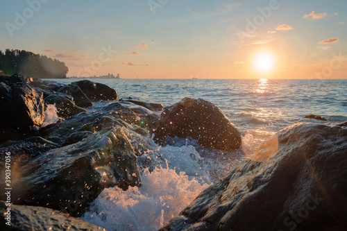 Sea waves crushing over the big rocks with beautiful sunset sky and city line on the background