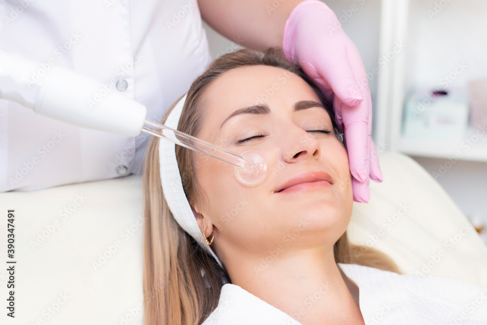 Cosmetologist performs a pulse current procedure for the face of a young woman. Cosmetologist performs a pulse current procedure for the face of a young woman.