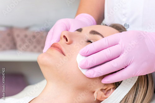 cosmetology. Close up picture of lovely young woman with closed eyes receiving facial cleansing procedure in beauty salon.