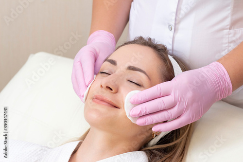 cosmetology. Close up picture of lovely young woman with closed eyes receiving facial cleansing procedure in beauty salon.