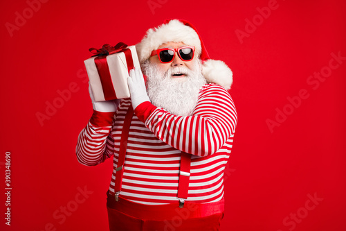 Portrait of his he nice handsome attractive bearded cheerful Santa father holding in hands giftbox guessing what's inside idea isolated bright vivid shine vibrant red color background