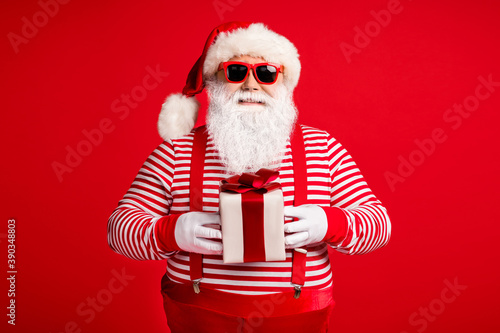 Portrait of his he nice handsome attractive cheerful cheery Santa Saint Nicholas holding in hands giftbox festal day occasion isolated bright vivid shine vibrant red color background © deagreez