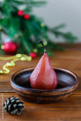 Poached pear in red wine with spices on the background of a Christmas tree.