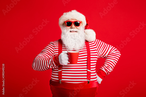 Portrait of his he nice attractive handsome cheerful cheery Santa drinking cacao latte holly jolly festal good mood isolated on bright vivid shine vibrant red color background © deagreez