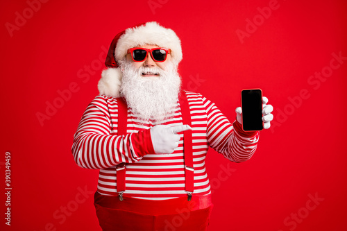 Portrait of his he nice handsome cheerful bearded fat Santa holding in hand demonstrating gadget 5g app shopping service sale order delivery isolated on bright vivid shine vibrant red color background © deagreez
