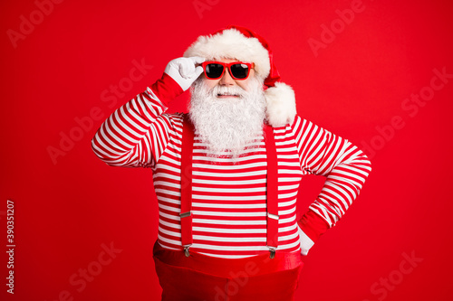 Portrait of his he nice handsome cheerful cheery grey-haired Santa wearing touching sunglasses winter good festal mood isolated over bright vivid shine vibrant red color background © deagreez