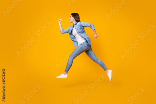 Full length body size profile side view of her she nice slim cheerful cheery girl jumping running fast speed active lifestyle regime isolated bright vivid shine vibrant yellow color background © deagreez