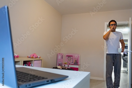 businessman working at home reaching his table with laptop, coffee in hand and yawning because he is just awake