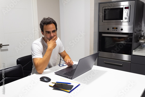 thinking businessman working at home from the kitchen with his laptop