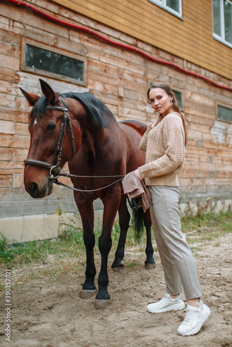 Girl rider standing next to the horse. The girl holds the horse's bridle