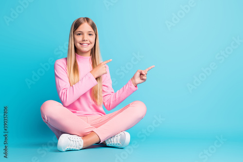 Photo of cheerful nice blond teen girl sit lotus point empty space dress pink pants poloneck isolated on teal background photo