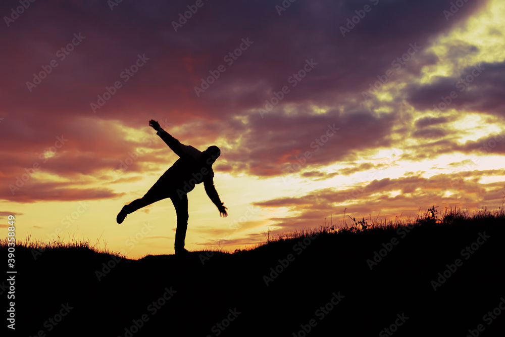 silhouette of a man standing on one leg and balancing trying to maintain balance