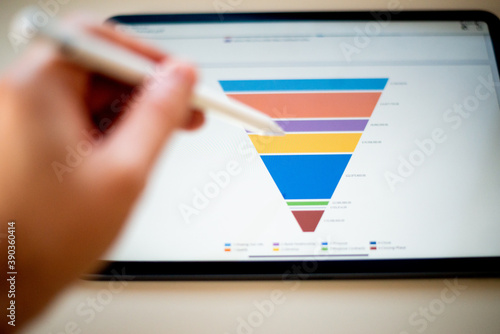 Sales marketing funnel showed on a tablet screen by a young marketer, sales manager pointing data with his pen.