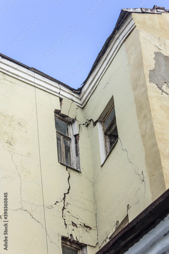 The old house is crumbling. Cracks run along the wall and windows. Photo for a site about architecture and restoration of old houses.