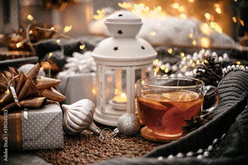 Beautiful Christmas still life. A cup of hot tea with a knitted sixth blanket on a warm floor among New Year's gifts and lights. Cozy flatlay. Christmas home cooking concept