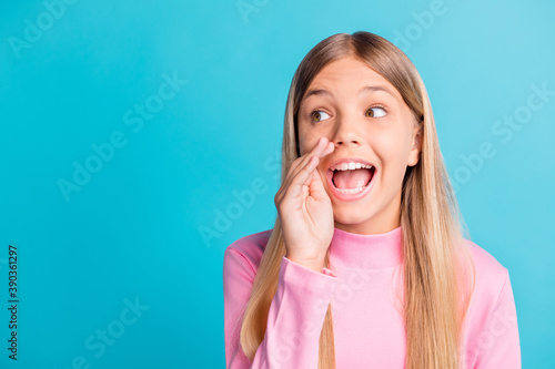 Photo portrait of schoolgirl with blonde hair telling secret quietly looking at blank space isolated on vibrant teal color background
