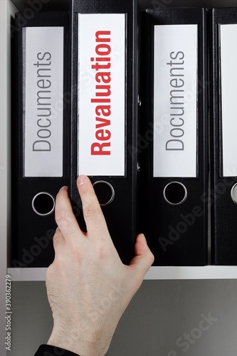 Revaluation. File Folder is taking by a hand from office shelf. Red Text is on the label of the documents. photo