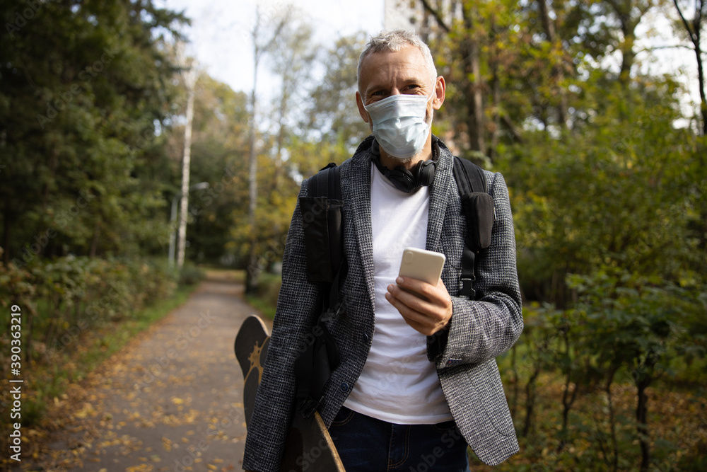 Cheerful mature male in mask walking with smartphone in wood Cheerful mature male in mask walking with smartphone in wood