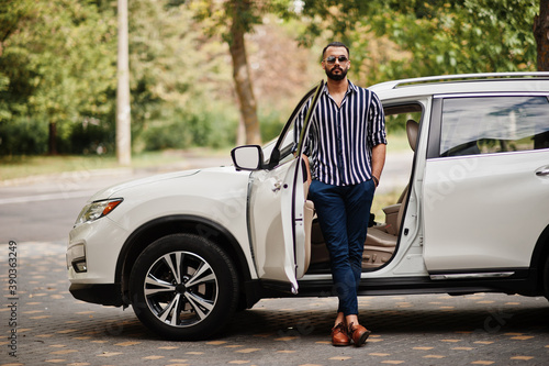 Successful arab man wear in striped shirt and sunglasses pose near his white suv car. Stylish arabian men in transport. © AS Photo Family