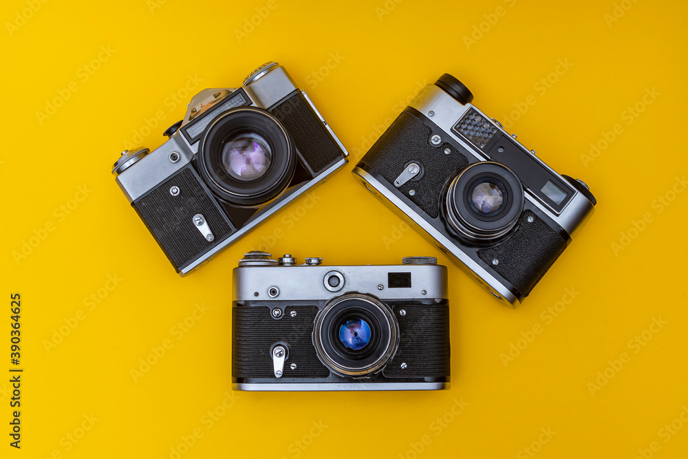 Three old film cameras lie on a yellow background in the shape of a triangle