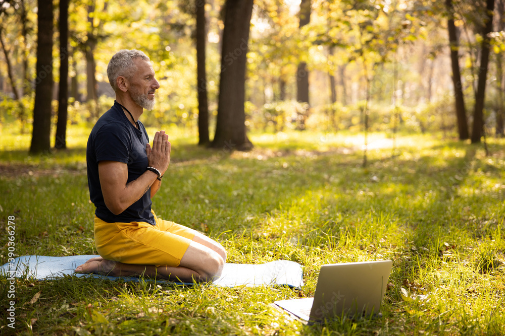 Calm mature male doing meditation with laptop outdoors - obrazy, fototapety, plakaty 