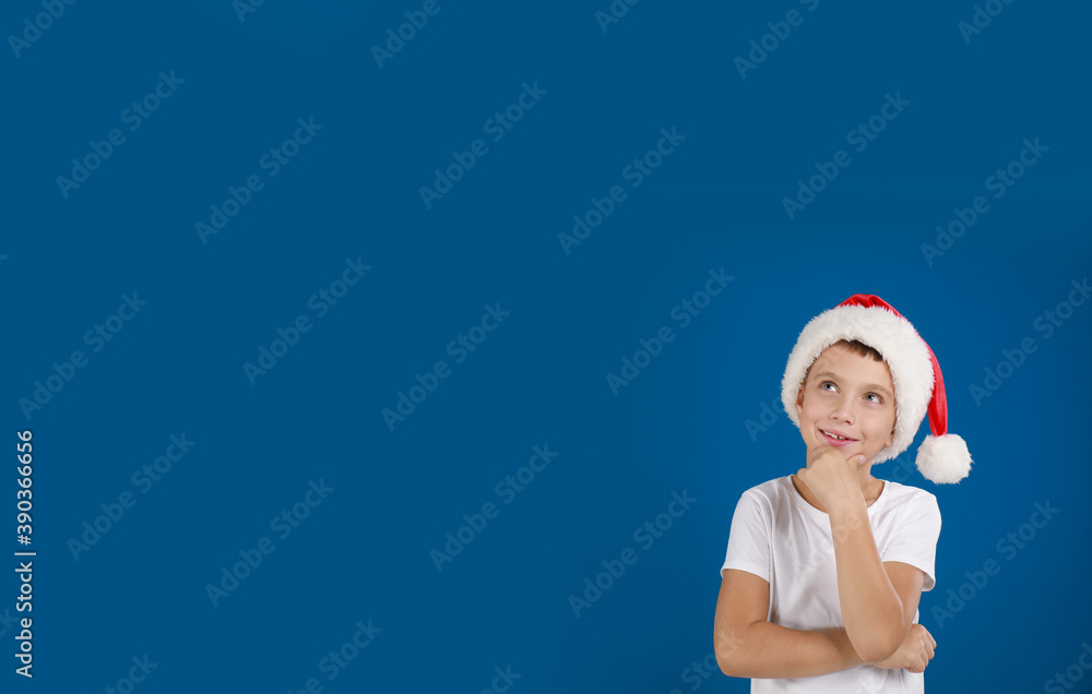 Thoughtful little child in Santa hat on blue background, space for text. Christmas celebration Thoughtful little child in Santa hat on blue background, space for text. Christmas celebration
