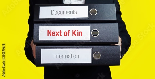 Next of Kin. Man carries stack of folders. File folders with text label. Background yellow.