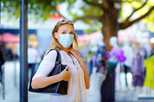 Portrait of young beautiful woman wearing medical mask as protection against corona virus. Woman shopping in the city. Covid pandemic time in Europe and in the world. Safety for people. © Irina Schmidt