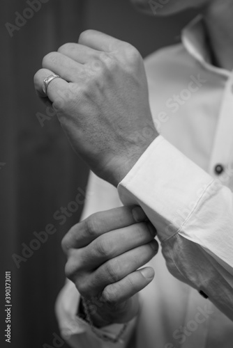 The man fastens the cuffs of the shirt. Morning of the groom. Hands of wedding groom buttoning up his white shirt. Male's hands on a background of a white shirt, sleeve shirt with cufflinks. Close-up