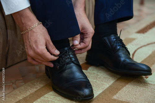 The man ties the shoelaces on the shoes. Business formal style of clothing. Official event. Wedding. Morning of the groom. Cropped image