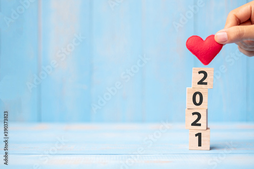 Business man hand holding red heart shape over 2021 wooden cubes on blue table background with copy space for text. Business, Resolution, New Year New You and Happy Valentine’s day holiday concept